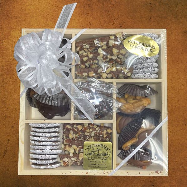 Wooden tray with 5 compartments containing butter crunch, nonpareils, chocolate caramel nut clusters and chocolate nut clusters, and a box with chocolate covered Oreos in the center.