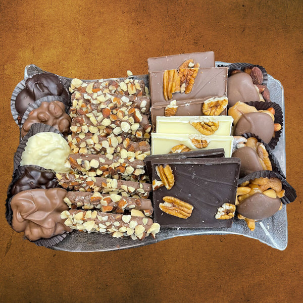 Large plastic tray with an assortment of buttercruch, pecan bark, chocolate caramel nut clusters, and chocolate nut clusters.