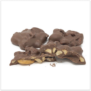 Milk chocolate cashew cluster cut in half in front of two other cashew clusters
