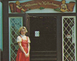 Woman in a red dress standing in front of a building with 'Welcome to Kellerhaus' sign.