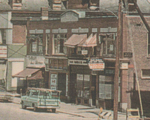 Damaged buildings on a city street with debris and vehicles in the foreground.