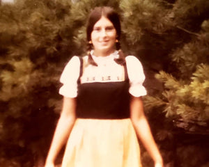 Person wearing a black top and yellow skirt standing outdoors with greenery in the background