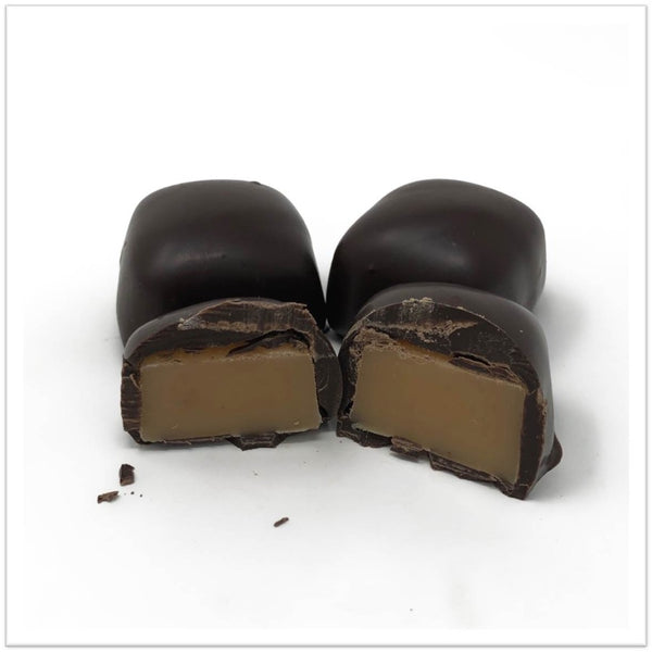 Dark chocolate covered butterscotch caramel cut in half in front of two other butterscotch caramels