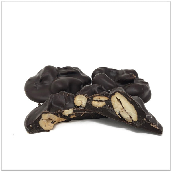 Dark chocolate cashew cluster cut in half in front of two other cashew clusters